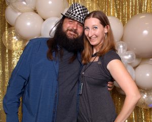 A couple smiling for the photo booth in front of a balloon garland and sparkly backdrop
