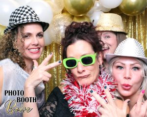 A group of women in fun hats and glasses taking a selfie in the photo booth