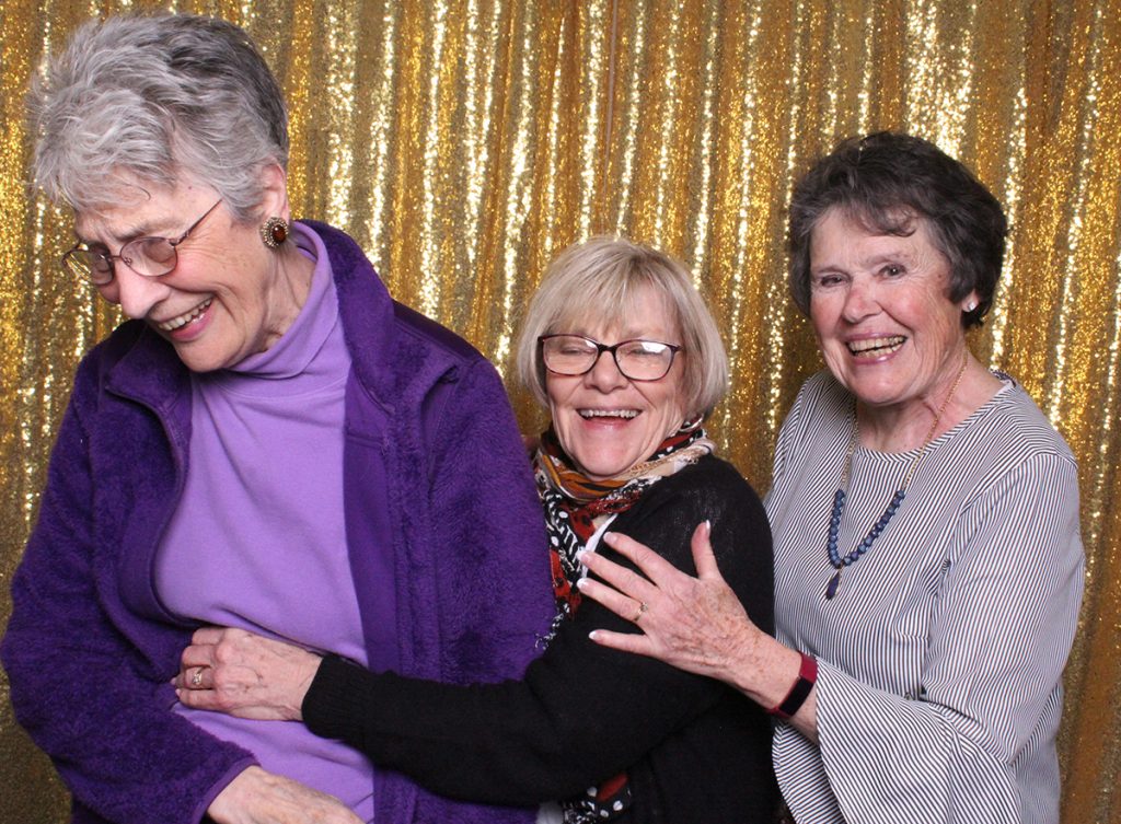2 ladies pulling their laughing friend back in the photo booth for more photos