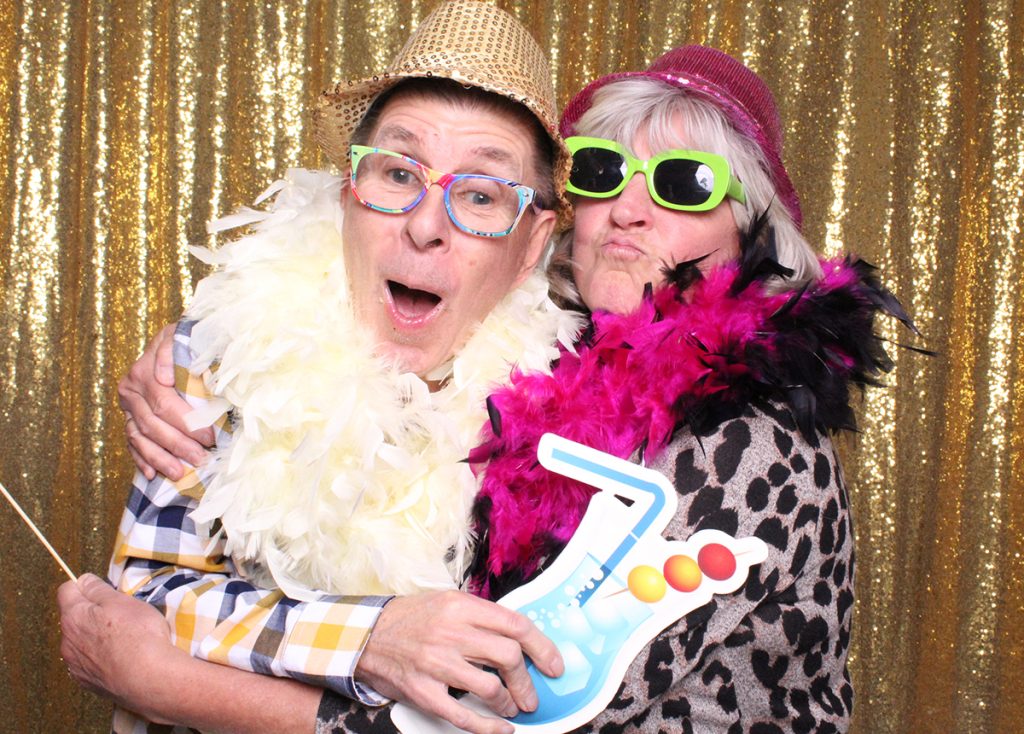 A silly couple with lots of props taking a selfie in the photo booth