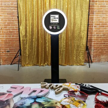 Social media sharing photo booth set up in front a of a gold sequin backdrop with a table full of fun photo booth props in front of it. 