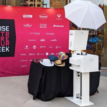 Open Air DSLR Booth set up with a table full of props in front of a corporate sponsored backdrop.